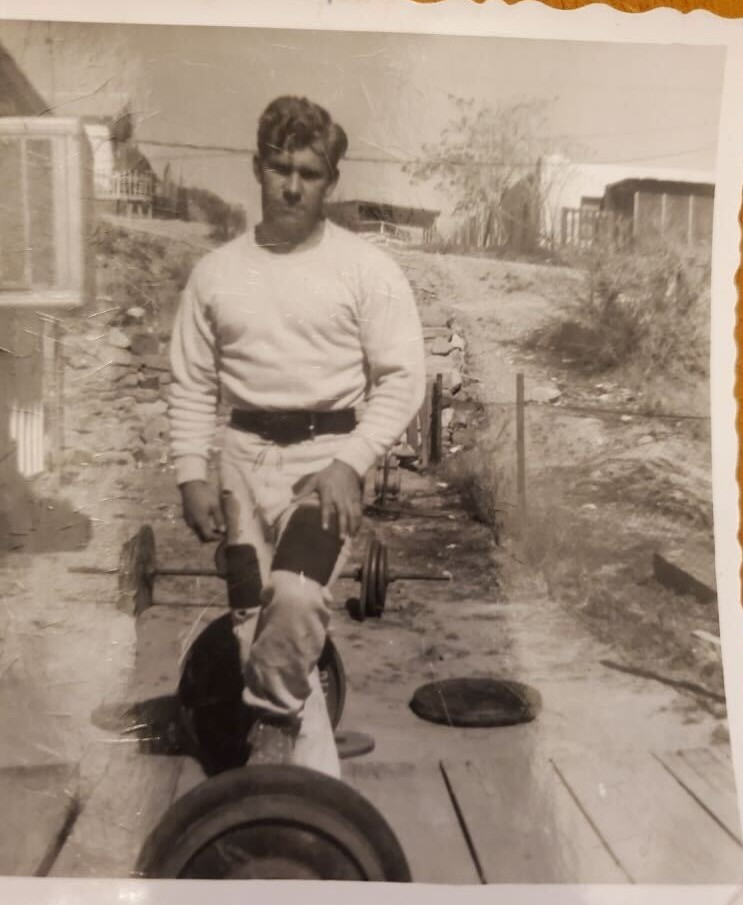 Young Gail Crick sitting outdoors near weights
